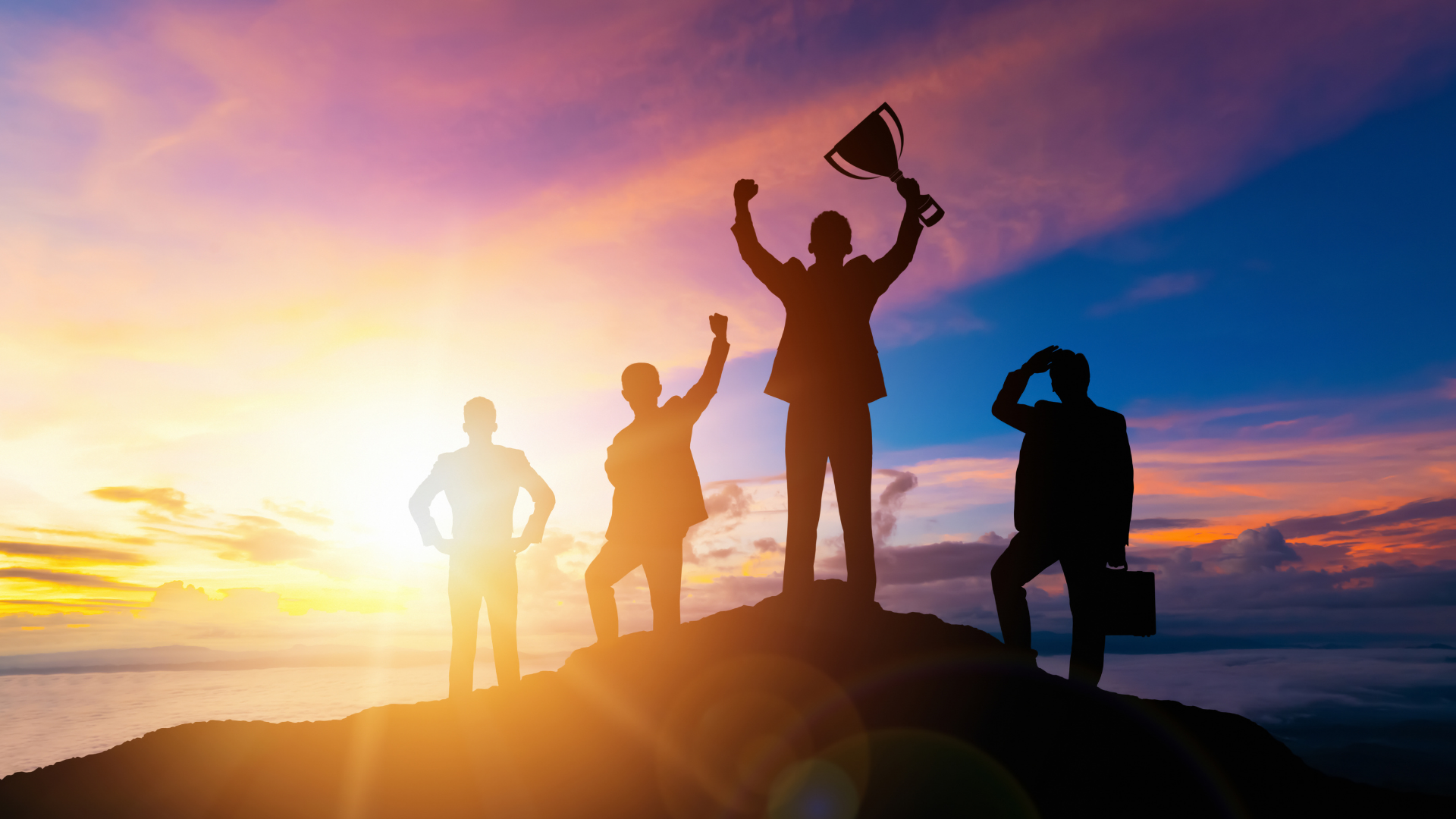 Silhouettes of business professionals celebrating success against a dramatic sunset sky, representing teamwork and achievement